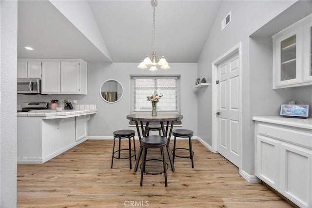 dining area with lofted ceiling, light hardwood / wood-style floors, and a chandelier