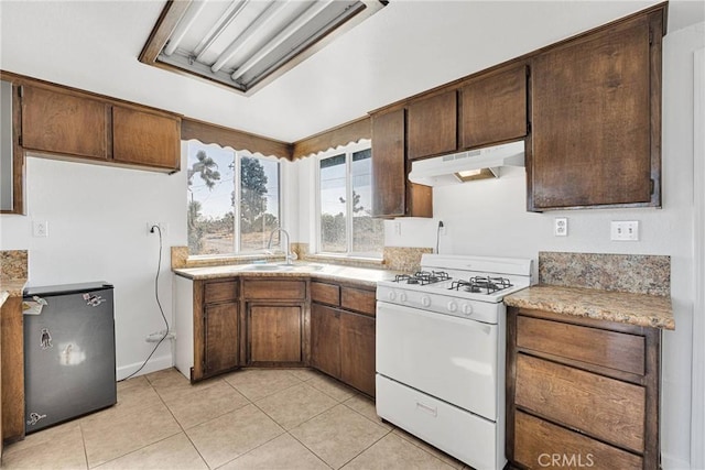 kitchen featuring sink, light tile patterned floors, stainless steel refrigerator, and gas range gas stove