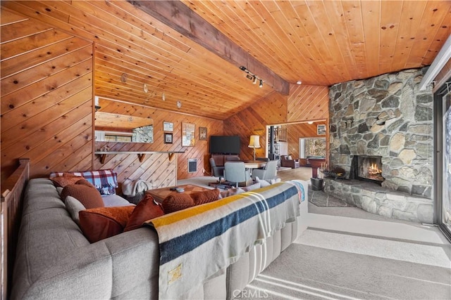 living room featuring a stone fireplace, wood walls, rail lighting, vaulted ceiling with beams, and wood ceiling