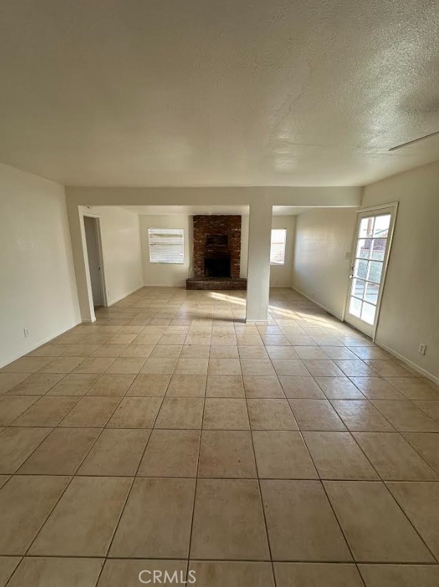 unfurnished living room with a brick fireplace, light tile patterned floors, and a textured ceiling