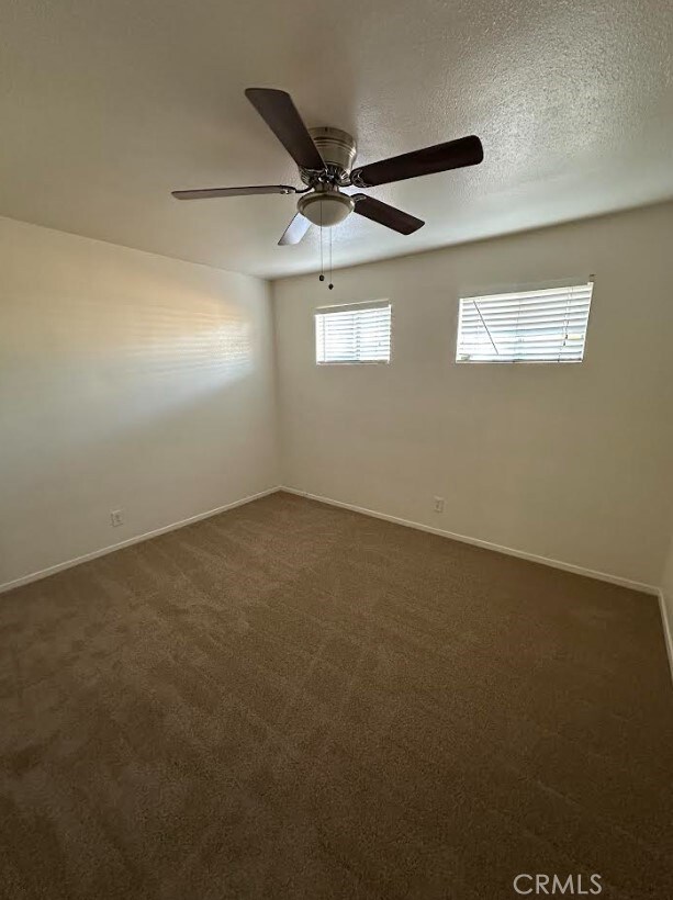 unfurnished room with ceiling fan, a textured ceiling, and dark colored carpet