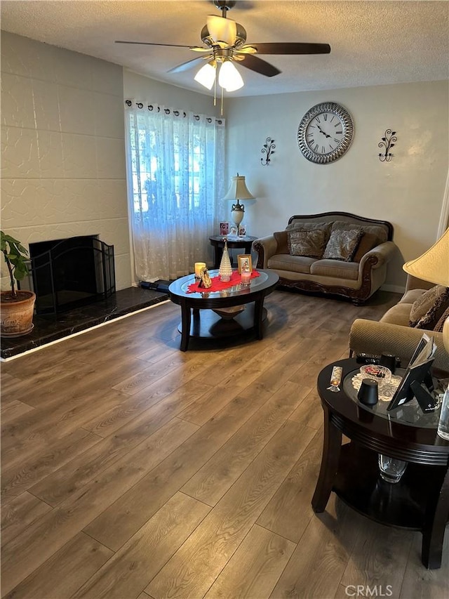 living room featuring a tiled fireplace, hardwood / wood-style floors, a textured ceiling, and ceiling fan