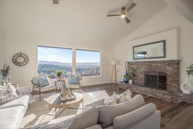 living room featuring a stone fireplace, high vaulted ceiling, hardwood / wood-style flooring, ceiling fan, and a mountain view