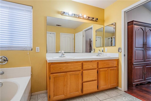 bathroom featuring a relaxing tiled tub, vanity, and tile patterned flooring