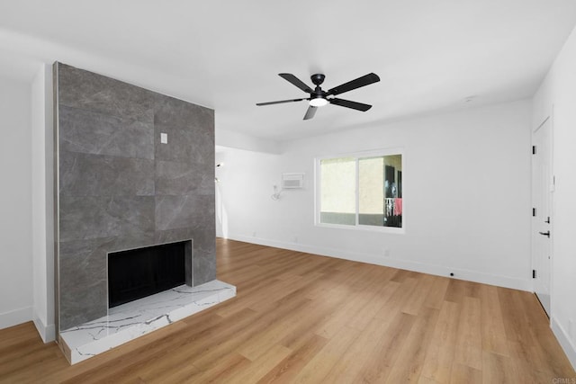 unfurnished living room with a wall mounted air conditioner, a fireplace, ceiling fan, and light wood-type flooring