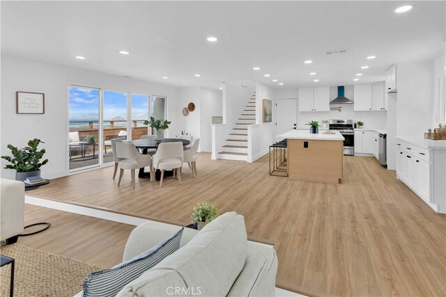 kitchen with white cabinetry, stainless steel appliances, a center island, light hardwood / wood-style floors, and wall chimney exhaust hood