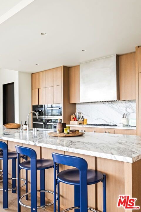 kitchen with a kitchen breakfast bar, light stone counters, decorative backsplash, kitchen peninsula, and light brown cabinets