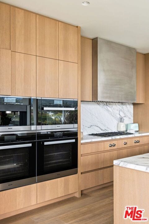 kitchen featuring double wall oven, light stone countertops, stainless steel gas cooktop, light brown cabinets, and light wood-type flooring