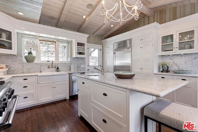 kitchen with high end appliances, white cabinetry, sink, and hanging light fixtures