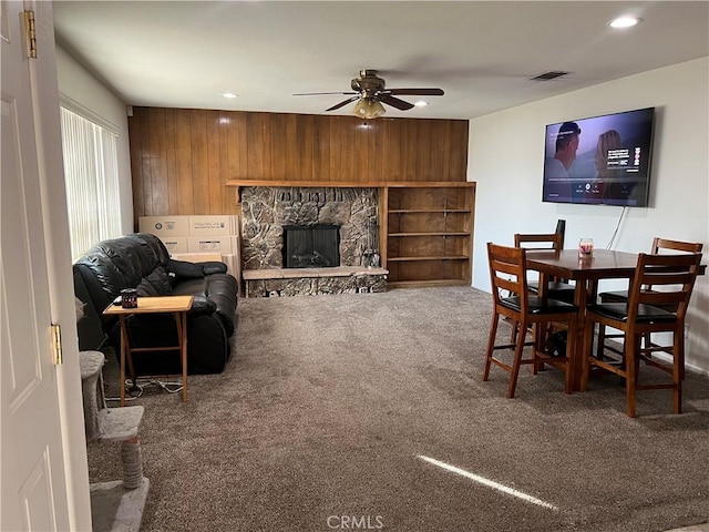 dining space with ceiling fan, carpet, a fireplace, and wooden walls