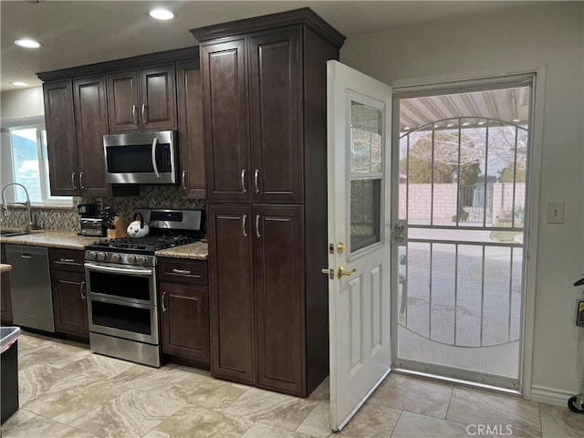 kitchen featuring sink, appliances with stainless steel finishes, dark brown cabinetry, tasteful backsplash, and light stone countertops