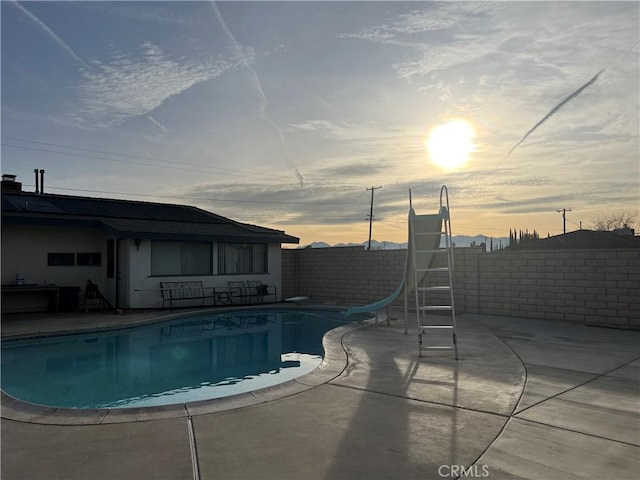 pool at dusk featuring a water slide and a patio