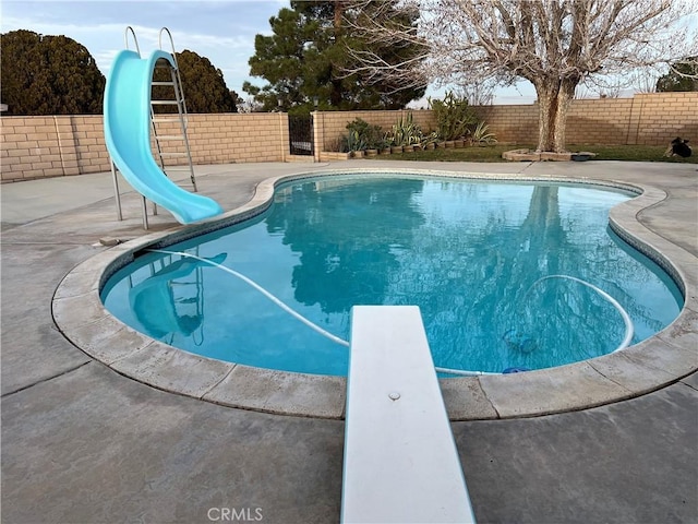 view of pool with a water slide, a diving board, and a patio area