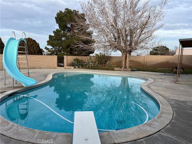 view of swimming pool with a water slide, a diving board, and a patio area