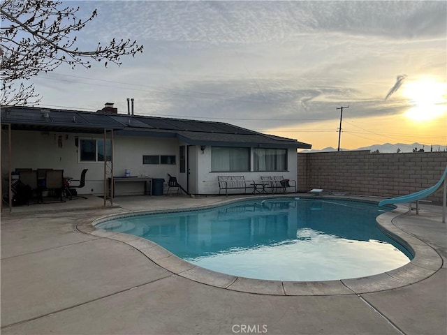 pool at dusk featuring a water slide and a patio area