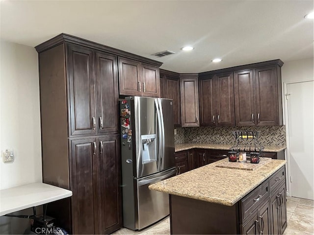 kitchen featuring dark brown cabinetry, tasteful backsplash, stainless steel fridge, a kitchen island, and light stone countertops