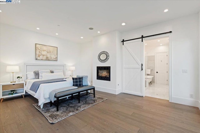 bedroom featuring ensuite bath, wood-type flooring, and a barn door