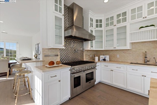 kitchen featuring double oven range, white cabinets, sink, and wall chimney exhaust hood