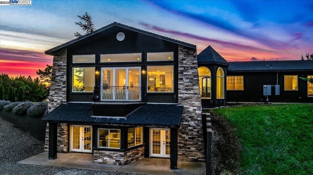 back house at dusk featuring french doors and a yard