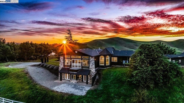 back house at dusk with a mountain view, a lawn, and a patio area