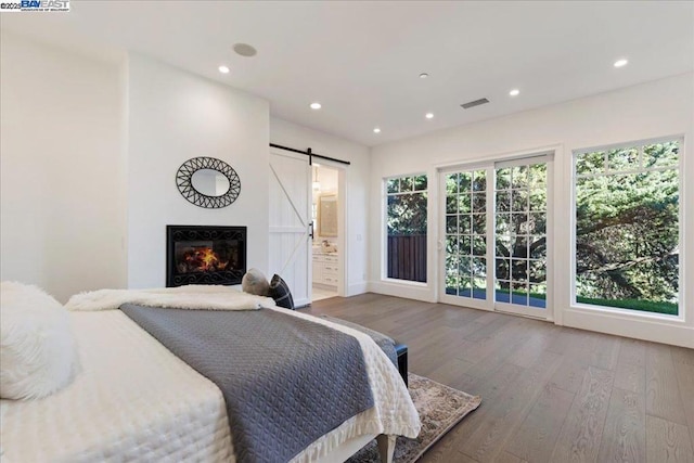 bedroom featuring hardwood / wood-style flooring, ensuite bathroom, a barn door, and multiple windows