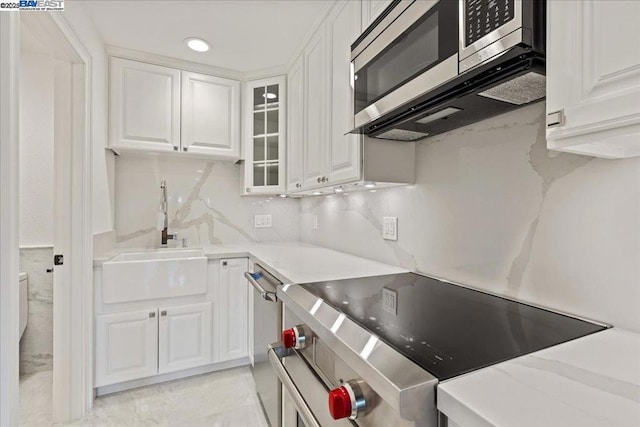 kitchen with sink, white cabinets, backsplash, stainless steel appliances, and light stone countertops