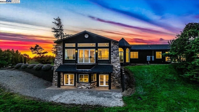 back house at dusk featuring a patio, a yard, french doors, and a balcony