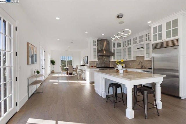 kitchen featuring a kitchen island, pendant lighting, white cabinets, built in refrigerator, and wall chimney exhaust hood