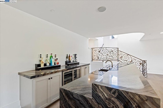 bar featuring wine cooler, dark stone counters, and white cabinets