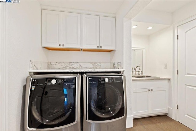 laundry area featuring cabinets, separate washer and dryer, sink, and light hardwood / wood-style flooring