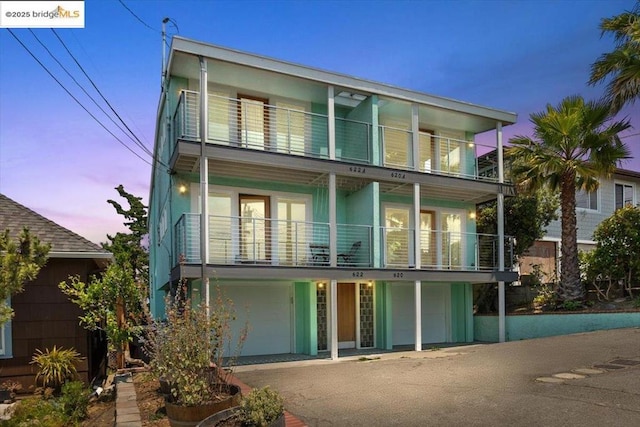 back house at dusk featuring a balcony and a garage