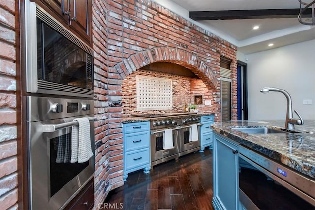 kitchen with sink, dark wood-type flooring, dark stone counters, and appliances with stainless steel finishes