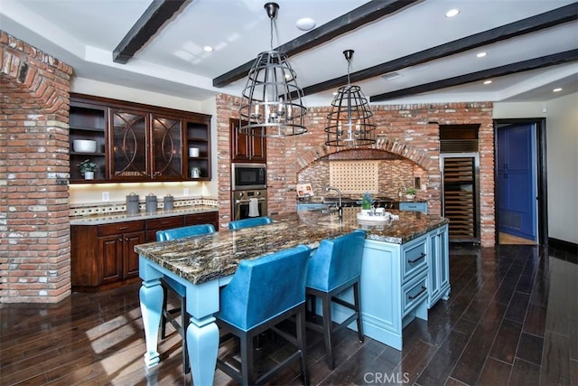 kitchen featuring black microwave, dark brown cabinets, a center island with sink, and oven