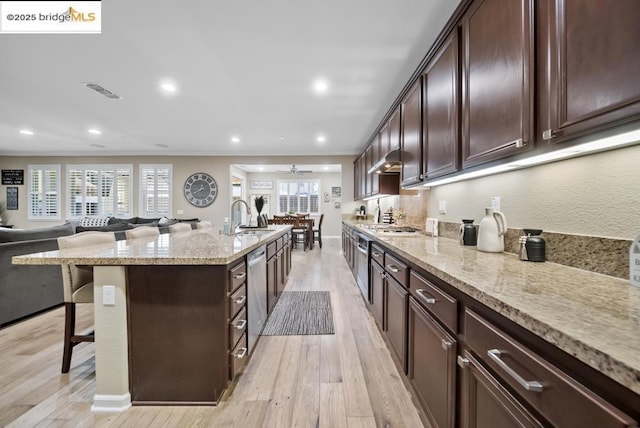 kitchen featuring sink, appliances with stainless steel finishes, a kitchen island with sink, light stone countertops, and a kitchen bar