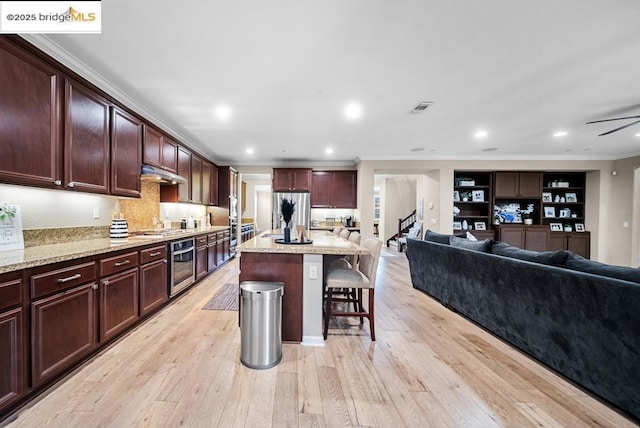 kitchen with a kitchen island, appliances with stainless steel finishes, a kitchen breakfast bar, light stone counters, and light hardwood / wood-style flooring