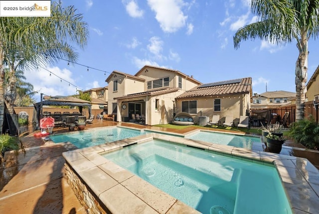 back of house with a gazebo, a swimming pool with hot tub, and solar panels