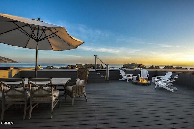 deck at dusk with a fire pit and a water view