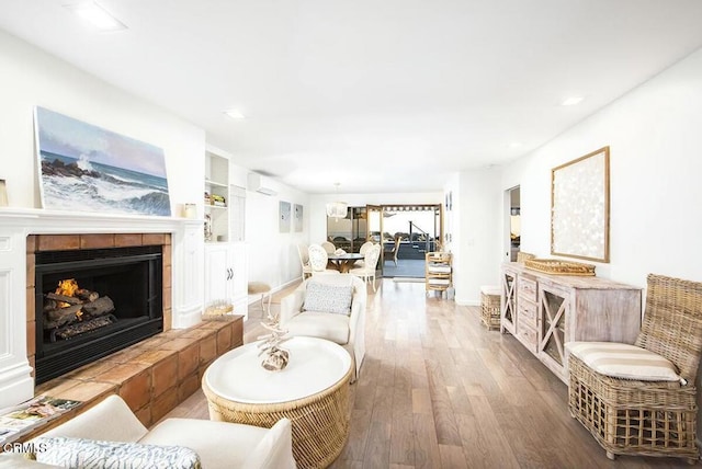 living room featuring hardwood / wood-style floors, a fireplace, built in features, and an AC wall unit