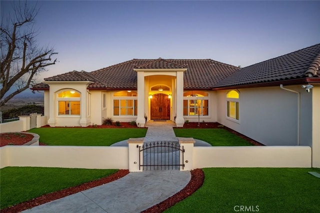 mediterranean / spanish house with a fenced front yard, a tile roof, stucco siding, a gate, and a front lawn