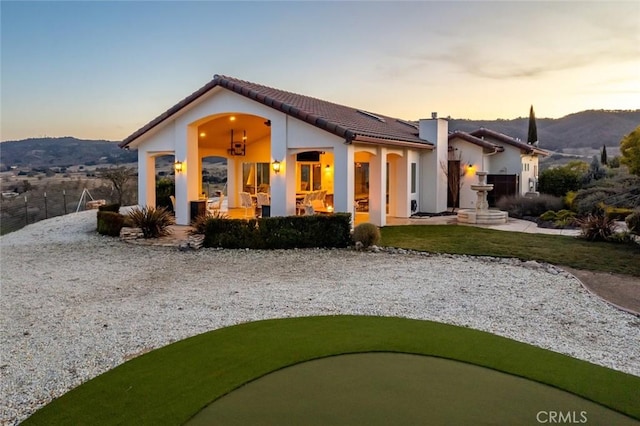 view of front of house with a patio, a tile roof, a chimney, a mountain view, and stucco siding