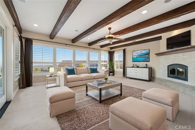 carpeted living room with a brick fireplace, beam ceiling, a healthy amount of sunlight, and ceiling fan