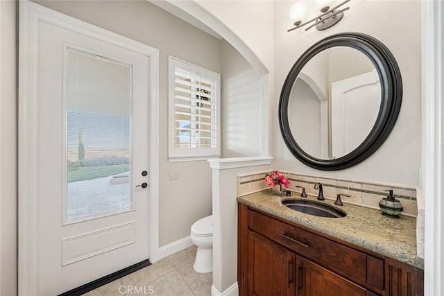 half bathroom with toilet, baseboards, vanity, and tile patterned floors
