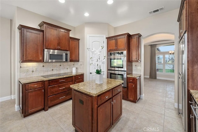 kitchen with baseboards, arched walkways, a center island, stainless steel appliances, and backsplash
