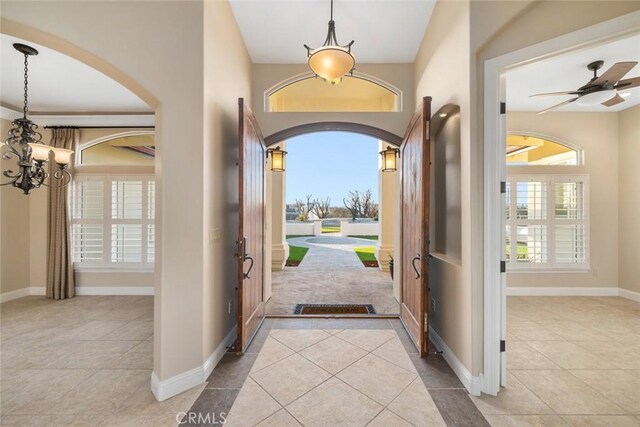 tiled foyer with arched walkways, baseboards, and ceiling fan with notable chandelier