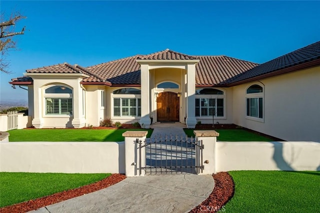 mediterranean / spanish home featuring a front yard, a tiled roof, a gate, and stucco siding