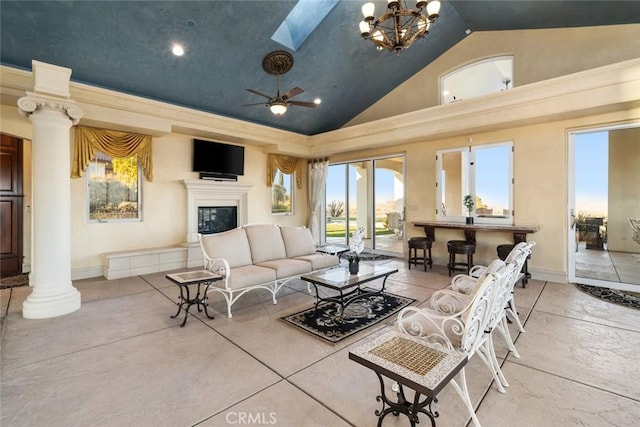 living room with ceiling fan with notable chandelier, a skylight, high vaulted ceiling, and ornate columns