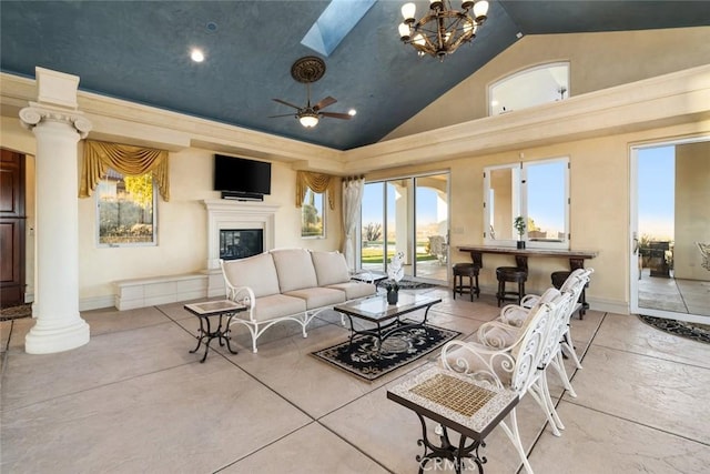 living area featuring a skylight, decorative columns, baseboards, a glass covered fireplace, and high vaulted ceiling