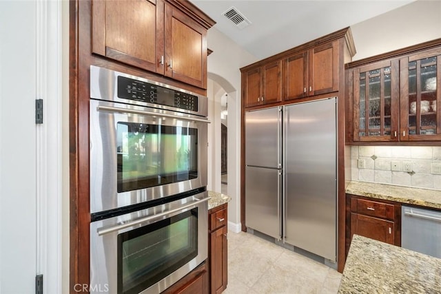 kitchen with appliances with stainless steel finishes, light stone countertops, and backsplash