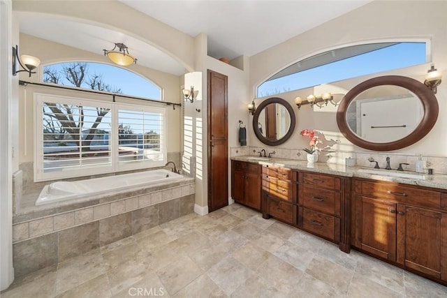 bathroom with vanity, tiled bath, and an inviting chandelier