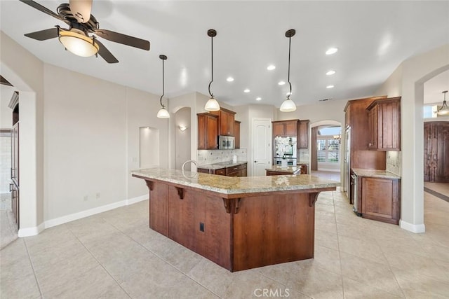 kitchen featuring pendant lighting, ceiling fan, stainless steel appliances, tasteful backsplash, and light stone countertops